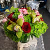 Bouquet of red roses, pink blooms, and green orchids in a glass vase