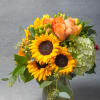 Bouquet of sunflowers, peach roses, and pale green hydrangea in a glass vase