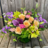 Mixed bouquet of peach, pink, purple, and green flowers in a glass vase