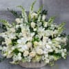 White floral arrangement in a woven basket with lilies and roses