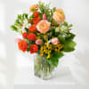 Mixed bouquet of orange and peach flowers in a clear glass vase