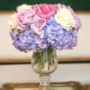 Pink and white roses arranged with lavender hydrangeas in a glass vase