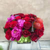 Red and pink flower arrangement with roses and peonies in a low container