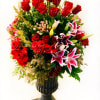 Tall arrangement of red roses and pink lilies in a dark pedestal vase