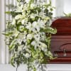 White funeral spray with lilies, roses, and daisies beside a casket