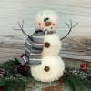 Small plush snowman with a striped scarf and wire arms on a rustic surface
