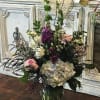 Tall mixed flower arrangement in a glass vase with purple, white, and pink blooms