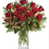 Red roses arranged in a clear glass vase with evergreen accents