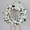 Large white floral wreath with lilies, roses, and daisies on a metal easel stand.