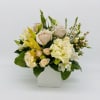 Low arrangement of cream roses and mixed white flowers in a square white vase