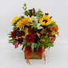 Square wooden vase arrangement with yellow sunflowers, red mums, white blooms, and orange accents.