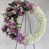 Large open wreath of purple and white flowers displayed on a black metal easel