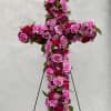 Standing floral cross of pink and burgundy blooms on a metal easel.