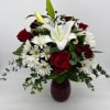 Red roses, white lilies, and white daisy mums arranged in a red glass vase