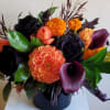 Orange and dark floral arrangement in a black vase with calla lilies and roses