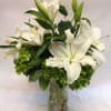 White lilies arranged in a clear glass vase with green blooms