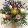 Mixed bouquet with protea, roses, and blue thistle in a burlap-wrapped vase