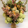 Tall mixed bouquet in a burlap-wrapped vase with peach, pink, and green blooms