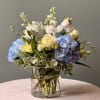 Blue hydrangeas and pale roses arranged in a clear glass vase