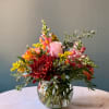 Mixed bouquet of pink, red, and orange flowers in a clear glass vase