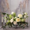 Cream and white floral arrangement in a silver bowl beside two lit candles