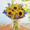 Bouquet of sunflowers, blue flowers, and yellow blooms in a glass vase