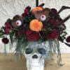 Halloween bouquet in a skull vase with red roses, orange dahlias, and eyeball accents