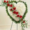 Heart-shaped floral spray with red roses and white flowers on a stand
