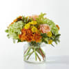 Bouquet of orange and yellow flowers with pale pink roses in a clear glass vase
