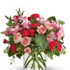 Pink roses and carnations in a clear glass vase with a succulent center