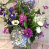 Tall mixed bouquet of purple, blue, pink, and white flowers in a clear glass vase