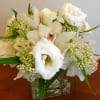 Low arrangement of white roses, lisianthus, and orchids in a clear glass cube vase