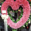 Pink heart-shaped floral wreath on an easel with a white ribbon bow