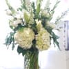 White floral arrangement in a tall glass vase with lilies and hydrangeas
