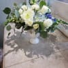 White floral arrangement in a white pedestal vase with blue accents