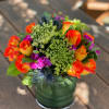 Bright mixed bouquet of orange roses and purple flowers in a glass vase