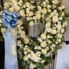 Large white floral funeral wreath with a blue ribbon on an easel