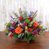 Colorful mixed flower arrangement with red roses and orange gerberas in a wicker basket.