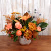 Autumn-toned arrangement with orange roses, lilies, and mums in a patterned ceramic vase