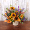 Mixed bouquet with sunflowers, red roses, and purple flowers in a cream vase