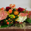 Low floral arrangement with pink anthuriums, orange roses, and white hydrangeas