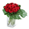 Red roses arranged in a clear glass vase with large tropical leaves