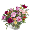 Short arrangement of pink roses, burgundy carnations, and peach blooms in a clear glass vase