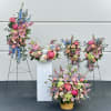 Large floral arrangements with pink, blue, and peach blooms in baskets and on stands