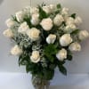 Tall arrangement of ivory roses with white filler flowers in a clear glass vase