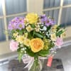 Bouquet of yellow roses, purple daisies, and pink carnations in a glass vase