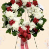 Red and white floral wreath with a red ribbon bow on a stand