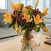 Orange lilies and burgundy daisies in a clear glass vase with a ribbon
