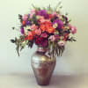 Mixed pink, purple, and orange flowers arranged in a metallic vase
