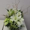 White lily arrangement in a dark round container with curly branches